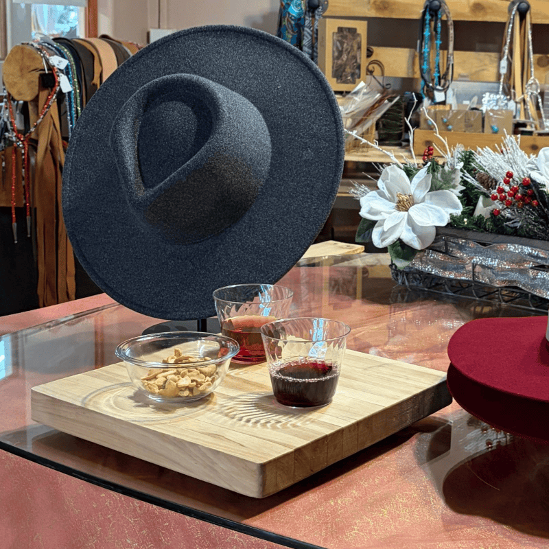 Black felt hat displayed on a table with drinks and holiday decor.